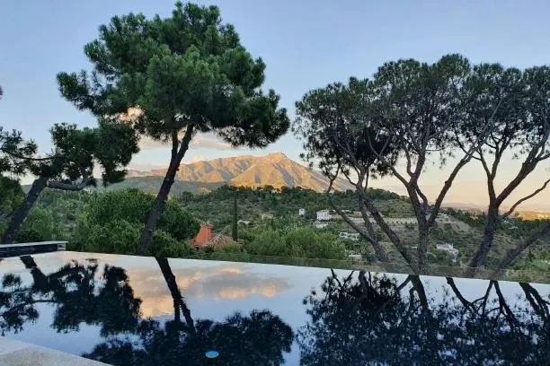 Exclusive luxury villas for sale in El Madroñal Benahavis. Looking over an infinity pool at la concha from a villa in el madronal. trees and sky reflected in the pool.